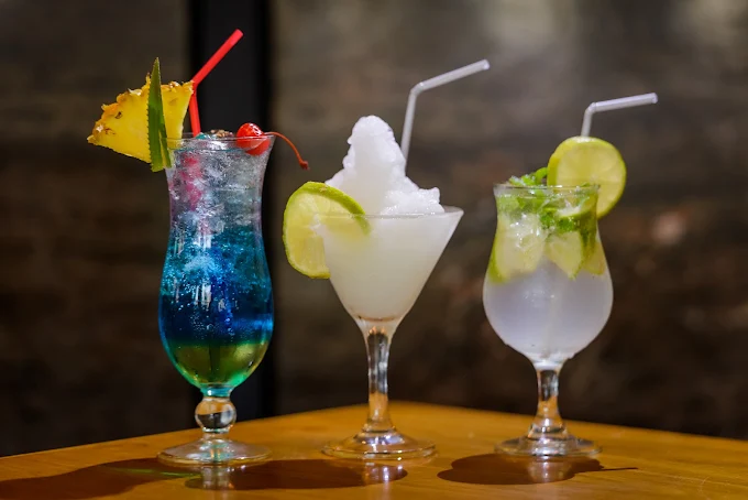 Three cocktails on a wooden table, garnished with pineapple, lime and mint