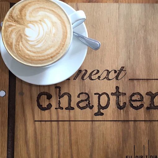 Latte with heart-shaped art on Next Chapter's branded wooden table